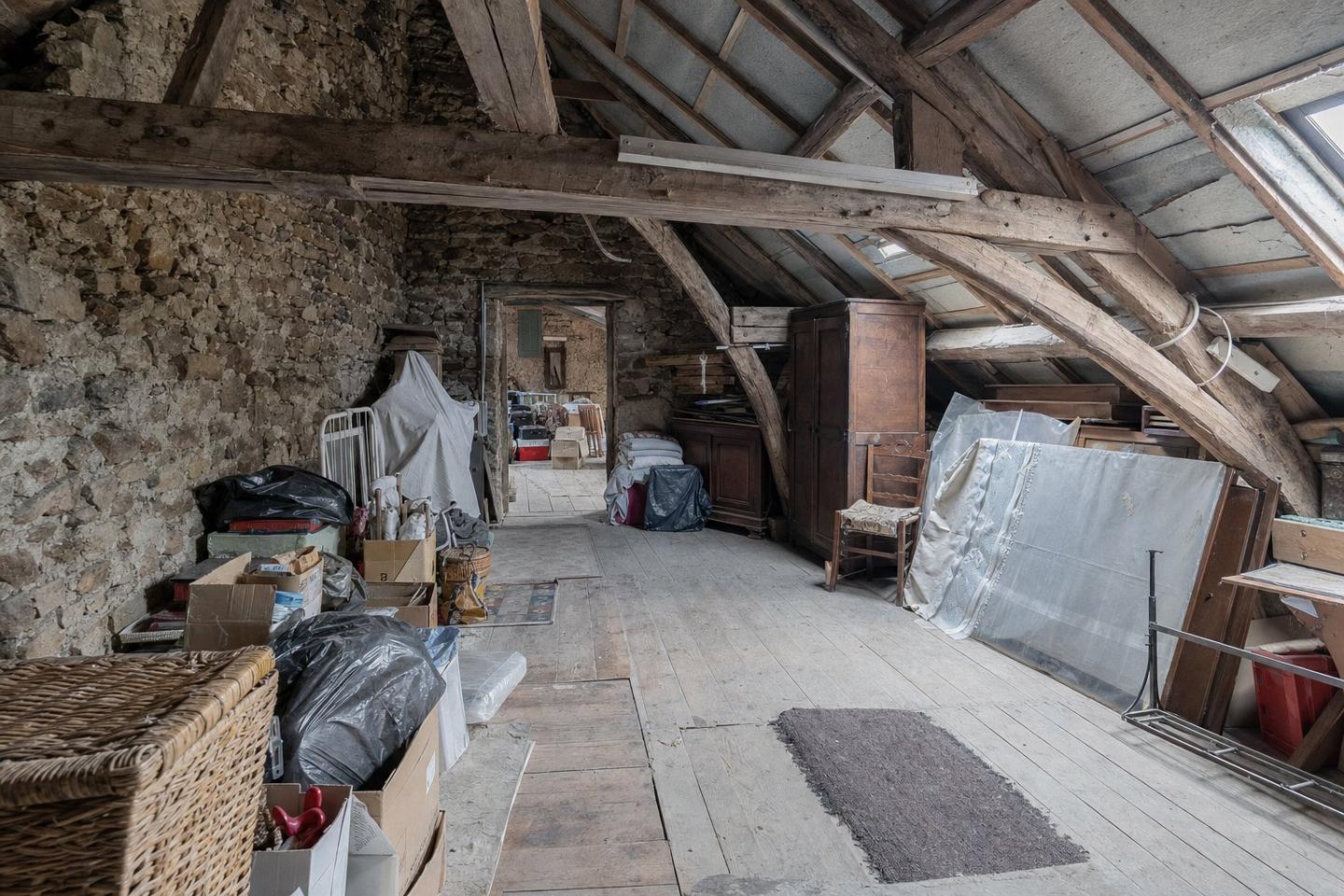 Maison ancienne en pierre avec soupirail de cave au ras du sol et lucarne de grenier sous un toit de tuiles, cartons et vieux meubles sortis devant la porte